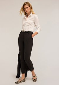 Camicia bianca a maniche lunghe, pantaloni neri aderenti e ballerine con stampa e dettagli dorati. Tessuto strutturato con design attillato e dettaglio della cintura.