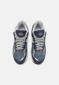 Granatowe i szare buty sportowe wykonane z siateczki i zamszu. Mają teksturowaną cholewkę, sznurowanie i białą gumową podeszwę. Widoczna marka New Balance.