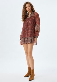 Mini dress merah dengan pola bunga, dilengkapi lengan panjang transparan dan hem berkerut. Memiliki kerah dan potongan santai. Sepatu bot pergelangan kaki suede.