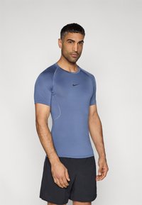 Εφαρμοστό μπλε αθλητικό μπλουζάκι από ύφασμα που απομακρύνει την υγρασία, με κοντά μανίκια και μαύρο λογότυπο Nike στο στήθος. Σετ με μαύρο σορτς.