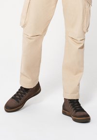 Brązowe sznurowane botki o teksturowanym wykończeniu i gumowych podeszwach, połączone z beżowymi spodniami cargo z bocznymi kieszeniami.