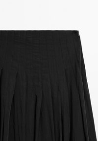 Jupe plissée noire taille haute avec des coutures verticales surpiquées et une fermeture éclair latérale sur fond blanc.