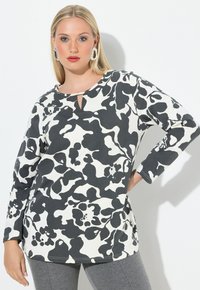 Langarm-Top mit abstraktem Blumenmuster in Schwarz und Weiß, mit Ausschnitt am Hals und weichem Baumwollstoff, kombiniert mit grauen Leggings.