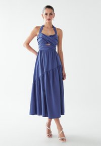 Brezrokavna, globoko modra obleka z nabrano pasom, zavito bodico in plastnim krilom. Tkanina je videti lahkotna z gladko teksturo.