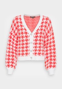 Czerwono-biały przycięty kardigan w jodełkę z długimi rękawami, zapinany z przodu na guziki przypominające przezroczyste kamienie, z prążkowanymi mankietami. Miękka faktura.