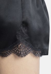 Shorts en satin noir avec une bordure en dentelle festonnée au bas, présentant des motifs complexes et une texture lisse.