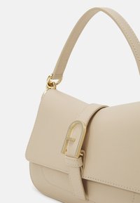 Beige leather handbag with a structured design, a gold metal clasp, and a short handle. Features stitched accents and a smooth texture.