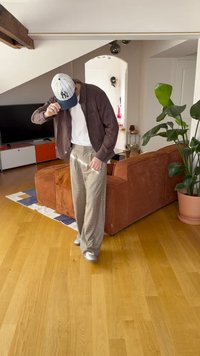 Barna kordbársony zakó fehér inggel, kockás bézs nadrág és világosszürke sportcipők. Benti környezet fa padlóval és növénnyel.