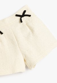 Hvide teksturerede shorts lavet af et vævet stof, med to sorte sløjfedetaljer på taljen og forlommerne.