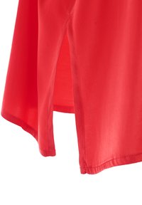 Indumento in tessuto rosso con una texture liscia, caratterizzato da spacco laterale e un orlo leggermente arrotondato. I punti di cucitura sono puliti e discreti.