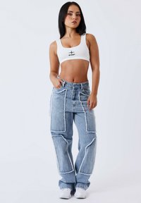Top corto bianco con logo nero, abbinato a jeans baggy azzurri chiari con toppe e bordi sfrangiati. Sneakers bianche completano il look.