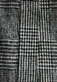 Tessuto a motivi in bianco e nero con un mix di quadretti e righe di diverse dimensioni, dalla consistenza morbida e dall'aspetto soffice.