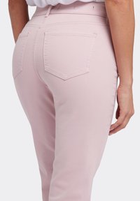 Jeans rosa claro con una textura suave, diseño de cinco bolsillos y detalles cosidos a lo largo de la cinturilla y los bolsillos.