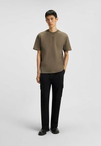 T-shirt verde oliva a maniche corte con scollatura rotonda, abbinato a pantaloni cargo neri con tasche laterali e una vestibilità comoda.