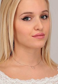 Collana in argento con un piccolo pendente circolare adornato con minuscole pietre preziose trasparenti, indossata su un collo nudo su uno sfondo chiaro.