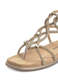 Sandal de color dorado con correas entrelazadas adornadas con pequeñas piedras decorativas. Plantilla suave y texturada y suela plana con un sutil brillo.