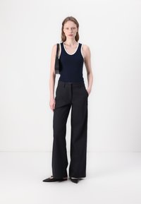 Navy tank top with white trim, paired with black wide-leg trousers and black pointed flats. Simple design with a smooth texture.