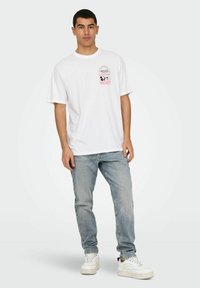 T-shirt en coton blanc avec un graphisme pastel et le texte "Mickey" sur la poitrine gauche. Associé à un jean en denim bleu clair et des baskets blanches.