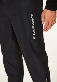 Zwarte waterdichte broek van nylon met een gladde textuur. Heeft witte "ENDURANCE" branding langs de zijkant.