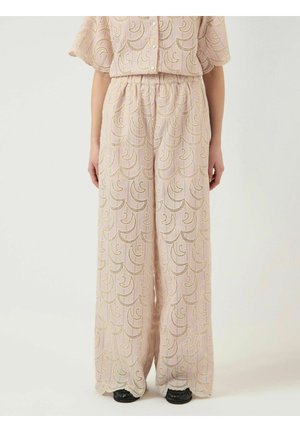 Leveälahkeiset pastellin vaaleanpunaiset housut, joissa on aaltoilevaa kultakirjailua, yhdistettynä saman sävyiseen yläosaan ja mustiin kenkiin yksivärisellä taustalla.