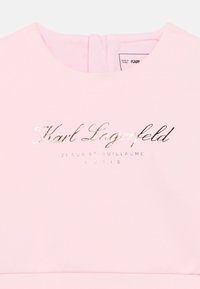 Ροζ υφασμάτινο τοπ με στρογγυλή λαιμόκοψη και μεταλλικό ασημένιο λογότυπο "Karl Lagerfeld" με διεύθυνσ η στο Παρίσι από κάτω.