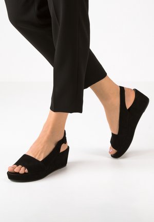 Czarne zamszowe sandały na koturnie z otwartym noskiem, z zapięciem na pięcie i teksturowanym wykończeniem. Obcas ma umiarkowaną wysokość, zapewniając wsparcie.