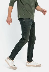 Donkergroene denim jeans met een slim fit, gecombineerd met witte sneakers met beige accenten. Het bovenstuk heeft lange mouwen en een relaxed model.