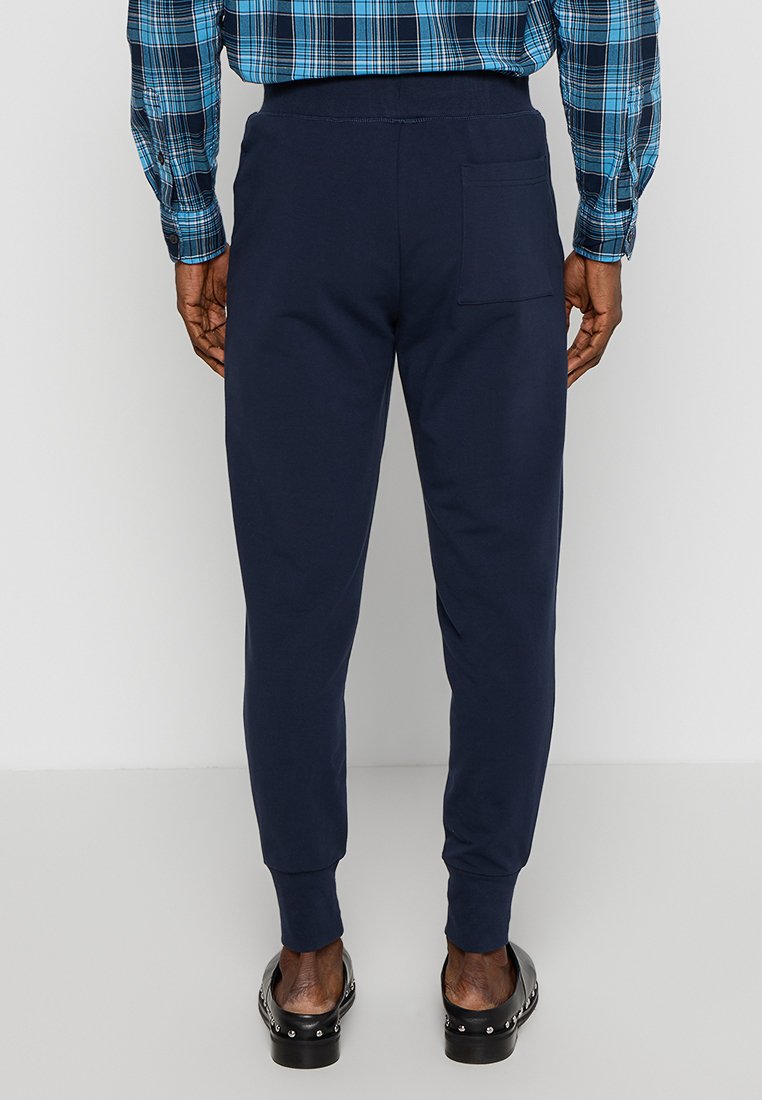Pantaloni jogger navy in tessuto morbido ed elastico con tasca posteriore, abbinati a una camicia a quadri blu. Presentano polsini a costine e una vestibilità comoda.