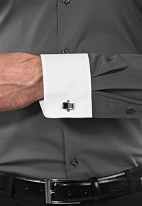 Camicia grigia con polsini bianchi a contrasto, dotata di un gemello nero e argento sul polsino destro. Tessuto morbido con vestibilità tailored.