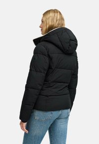 Chaqueta acolchada negra con capucha, con costuras horizontales, un forro interior blanco y un logo circular en la manga izquierda.