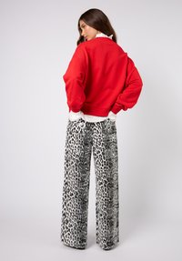 Punainen lyhyt collegepaita pyöreällä pääntiellä, yhdistetty leveälahkeisiin mustavalkoisiin leopardikuvioisiin housuihin, joissa on paljetilla koristeltu tekstuuri ja kuviot.