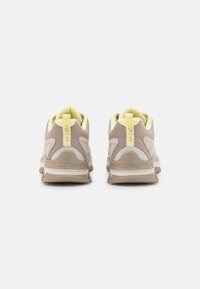 Beige athletic shoes featuring a mesh upper with yellow accents. Curved design, padded collar, and chunky rubber sole with branding detail.