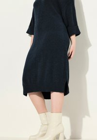 Abito di maglina navy con maniche a costine e spacchi laterali, abbinato a stivaletti con zeppa color crema dotati di chiusura a zip.