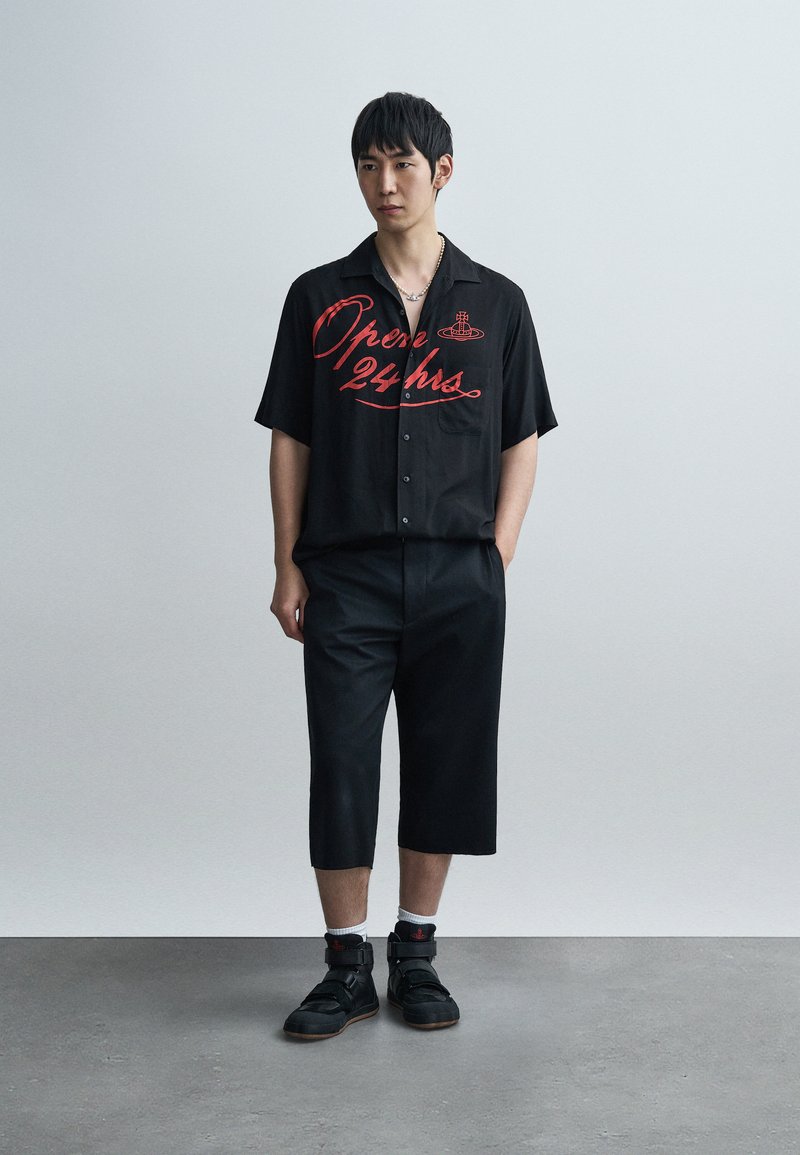 Chemise noire à manches courtes avec un motif rouge "Ouvert 24h/24", associée à un pantalon noir court et des baskets noires à sangles réglables.