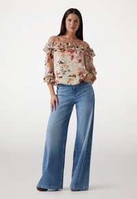 Off-the-shoulder floral blouse with ruffle trim, in light fabric; paired with high-waisted, wide-leg blue denim jeans. Brown heels.
