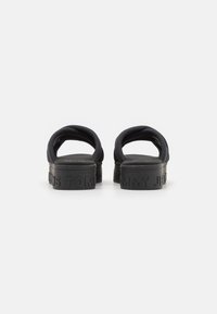 Schwarze Rutsch-Sandalen mit einer strukturierten Gummisohle und Stoffriemen. Auf der Rückseite befindet sich ein geprägtes Logo mit dem Markennamen.