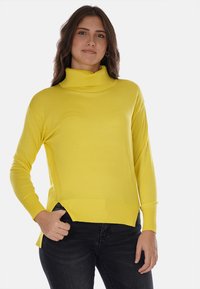 Maglione giallo a maniche lunghe con collo a dolcevita, orlo a coste e spacchi laterali, realizzato in materiale morbido e liscio, indossato con jeans scuri.
