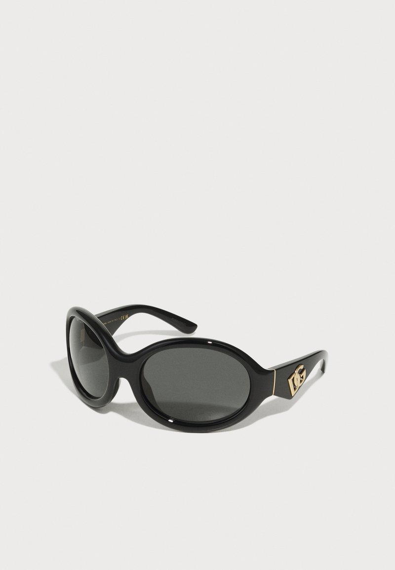 Occhiali da sole neri a forma ovale con lenti scure. Presentano una montatura in plastica lucida e accenti dorati del logo sui lati. Design leggero.