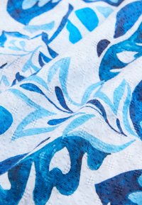 Tissu avec un fond blanc orné de motifs floraux bleus complexes, présentant différentes nuances et un tissage texturé.