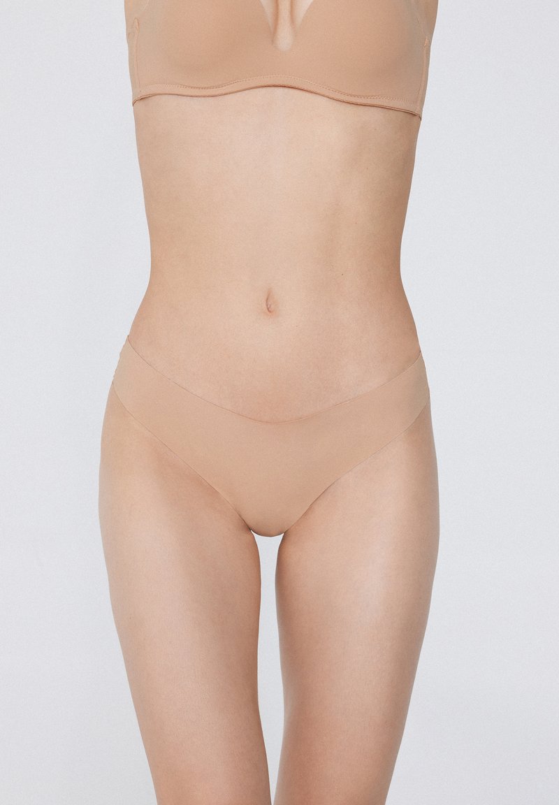 Nude bezszwowe stringi z cienką elastyczną talią i gładkim, lekkim materiałem, zaprojektowane z myślą o minimalnej widoczności pod odzieżą.