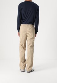 Beige cotton pants with a relaxed fit and elastic waistband, paired with a navy long-sleeve shirt. Footwear is white with dark accents.