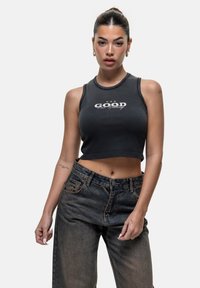 Top corto nero con una grafica che recita "GOOD" in bianco, abbinato a jeans in denim scuro a vita alta. Design e texture semplici.