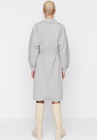 Hellgrauer Trenchcoat mit elastischem Bund, langen puffärmel, und knie-langer Schnitt, kombiniert mit beigen knielangen Stiefeln.