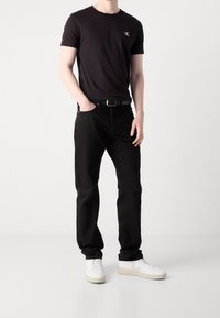 Czarny bawełniany T-shirt z okrągłym dekoltem i haftowanym logo, w zestawie z czarnymi dżinsami i białymi trampkami, z czarnym paskiem.