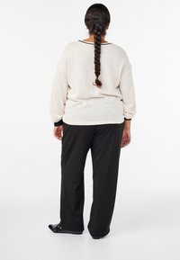 Gaiši bēša, pārliela džemperis ar garām piedurknēm un melnu apkakli. Kombinēts ar brīvi krītošām melnām biksēm un melniem apaviem.