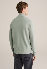 Mentolzeleni rebrasti džemper s visokim ovratnikom, dugim rukavima i uskim pojasom, upareni s tamnosivim trapericama.