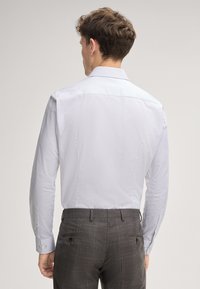Chemise habillée bleu clair, texturée, à manches longues, avec un col droit et des boutons blancs, assortie à un pantalon gris à motif.