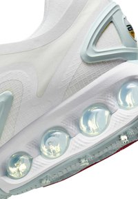 Lähikuva valkoisen urheilukengän pohjasta, jossa näkyy läpikuultavat ilmatyynyt ja teksturoitu verkkopäällinen muovituella.