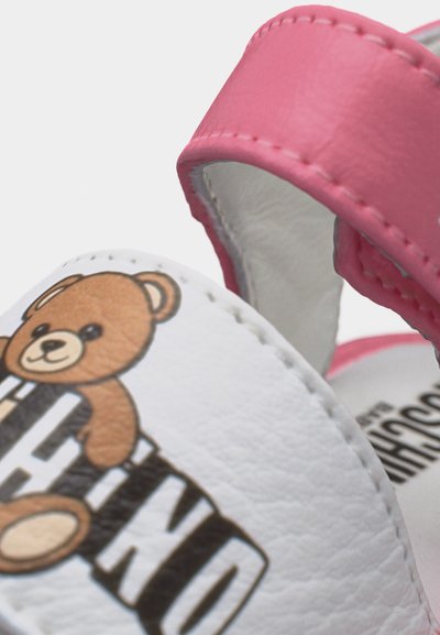 Λευκό και ροζ σανδάλι για νήπια με γραφικό αρκουδάκι και μαύρο έντονο κείμενο στο μπροστινό λουράκι, κοντινή λήψη που δείχνει τη ραφή και την υφή.
