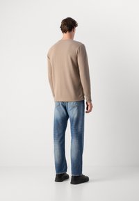 Beige langetermijnshirt met ronde hals, gecombineerd met lichtblauwe denim jeans. Eenvoudig ontwerp, regular fit en minimal zichtbare naden. Zwarte schoenen.